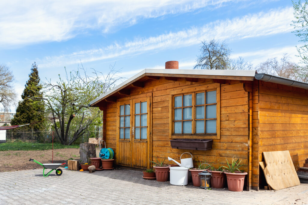 Small beautiful wooden house shed or storage hut for garden tools equipment and bicycles at backyard at beautiful american or european countryside backyard. Cozy rural yard stuff warehouse.