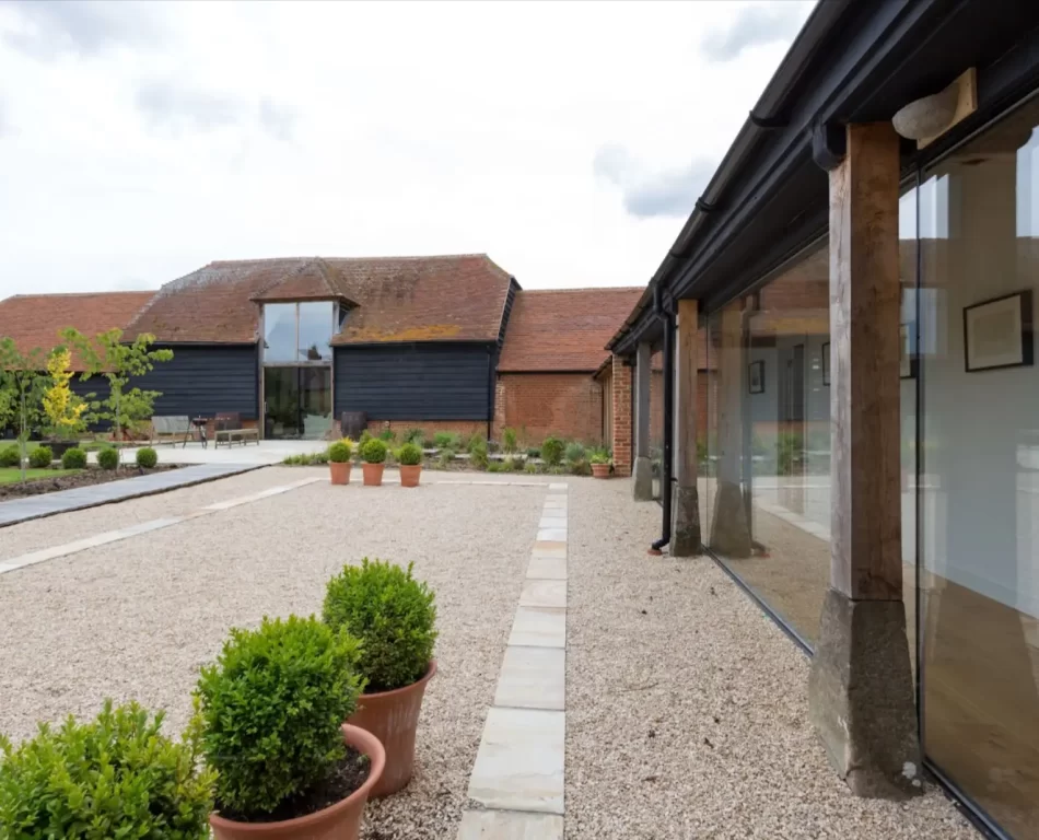 View of a patio along a house converted from a barn with glass windows.